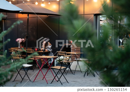 Enjoying a tranquil evening at an outdoor cafe surrounded by soft lights and greenery while wrapped in a cozy blanket on a cool night Enjoying a tranquil evening at an outdoor cafe surrounded by soft lights and greenery while wrapped in a cozy blanket on a cool night 130265154