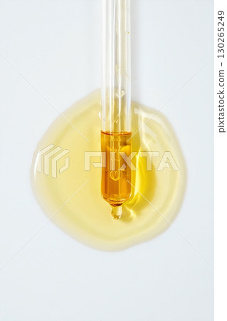 Serum dropper with golden amber liquid, creating a glowing puddle on surface, skincare product splash 130265249