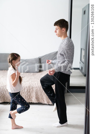 In a cozy living room filled with warmth and laughter, a young girl joyfully engages in dance lessons, eagerly learning new moves from her patient older brother, creating cherished memories together In a cozy living room filled with warmth and laughter, a young girl joyfully engages in dance lessons, eagerly learning new moves from her patient older brother, creating cherished memories together 130266108