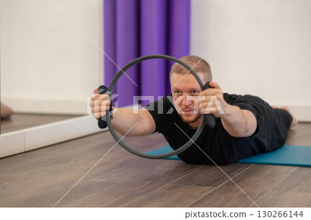 Male fitness Pilates trainer shows exercises on special simulators. Rubber rings for stretching. High quality photo Male fitness Pilates trainer shows exercises on special simulators. Rubber rings for stretching. High quality photo 130266144