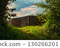 Vibrant sunset sky with shades of blue and pink and orangeover a rustic wooden fence surrounded by lush green grass and scattered clouds 130266201
