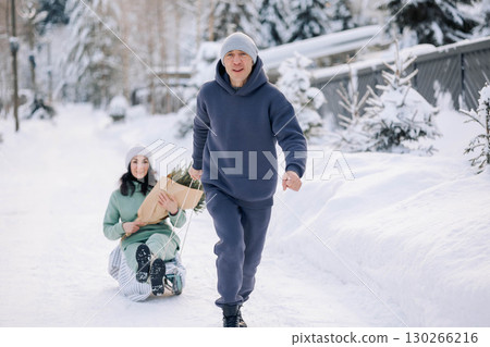 Smiling man giving sledding ride to woman. Love and leisure concept. High quality photo 130266216