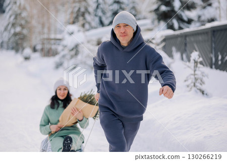 Smiling man giving sledding ride to woman. Love and leisure concept. High quality photo 130266219