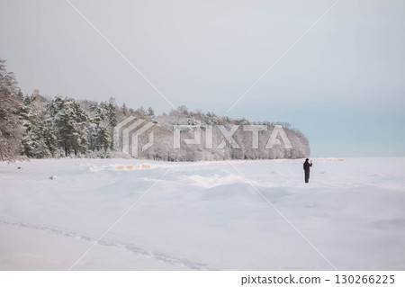 Beautiful winter landscape in minimalist style. Small figures of people on field of white snow and forest on horizon. Light and airy feel and light color palette. 130266225