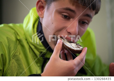 Enjoying a tasty slice of traditional rye bread while wearing a vibrant green jacket in a cozy indoor setting during a relaxed afternoon meal Enjoying a tasty slice of traditional rye bread while wearing a vibrant green jacket in a cozy indoor setting during a relaxed afternoon meal 130266435