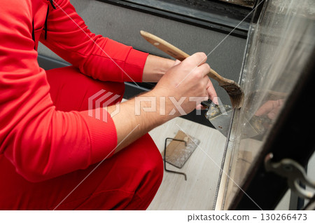 Crafting a new look with care, a person in a bright red outfit meticulously paints a surface in a cozy indoor space during the afternoon hours 130266473