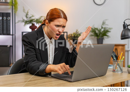 Young businesswoman frustrated laptop freezes hits table grabs head presses ctrl alt del for restart Young businesswoman frustrated laptop freezes hits table grabs head presses ctrl alt del for restart 130267126
