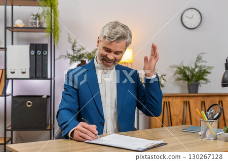 Middle-aged businessman signs document then dances laughing celebrating project completion triumph Middle-aged businessman signs document then dances laughing celebrating project completion triumph 130267128