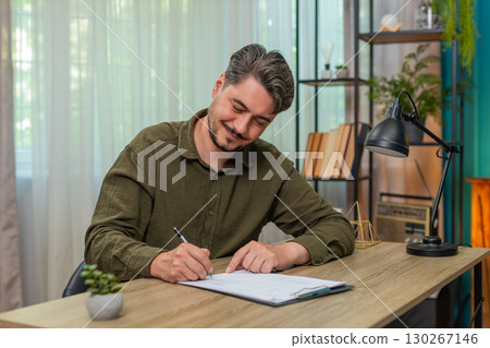 Middle-aged man satisfied signs documents approving content signing paperwork gladly at table desk Middle-aged man satisfied signs documents approving content signing paperwork gladly at table desk 130267146