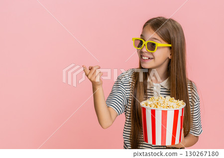 Child girl kid happily eating popcorn while watching funny cartoon laughing and smiling cheerfully 130267180