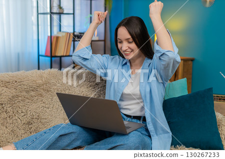 Woman emotionally celebrating success at laptop covering mouth surprised waving hands disbelief 130267233