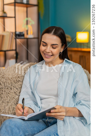 Young woman on sofa carefully writing notes in notebook thoughtfully making important todo list 130267236