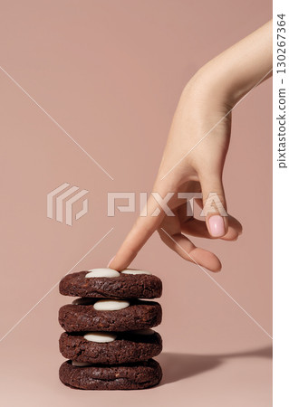 Chocolate cookies stacked with creamy filling, hand reaching for top cookie, bakery concept with copy space for menu design and promotional use 130267364