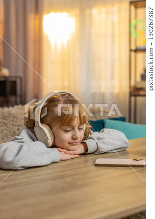 Young girl listening to audiobook with headphones, excitedly reacting to story with open eyes, smile 130267387