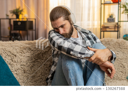Young man sad at home with headphones, melancholic music track, tearful mood quiet heartbreak moment 130267388