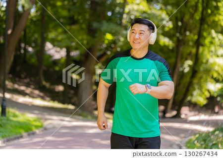 Active sportsman jogging training marathon run, listening to music in wireless headphones in park 130267434