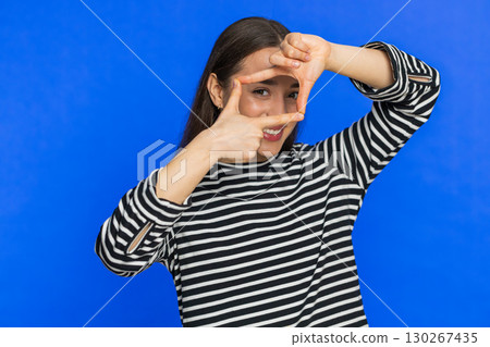Woman photographer gesturing picture frame with hands, looks through fingers focusing cropping image Woman photographer gesturing picture frame with hands, looks through fingers focusing cropping image 130267435