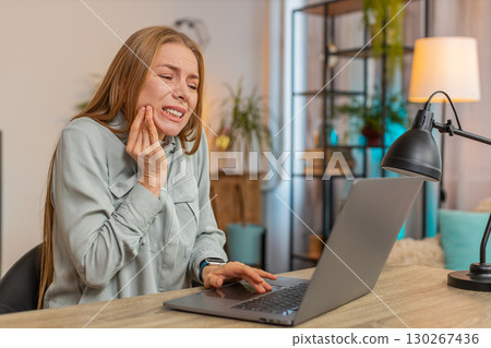 Caucasian woman freelancer sitting at home office table feeling toothache touching mouth at home 130267436