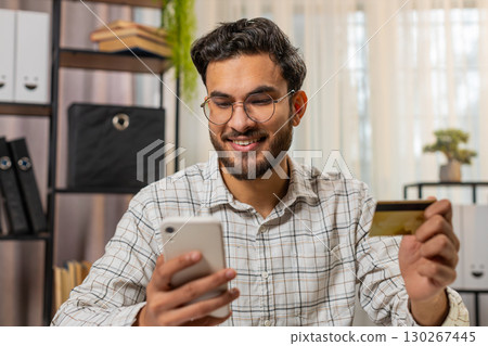 Happy Indian businessman using bank credit card and smartphone for online shopping bill payments Happy Indian businessman using bank credit card and smartphone for online shopping bill payments 130267445