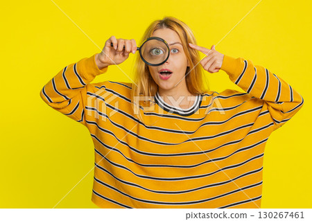 Young woman holds magnifying glass near face looking at camera with big zoomed eye, analyzing Young woman holds magnifying glass near face looking at camera with big zoomed eye, analyzing 130267461