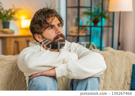 Sad frustrated young Indian man sitting at home looks pensive thinks over lonely life problems Sad frustrated young Indian man sitting at home looks pensive thinks over lonely life problems 130267468
