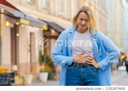 Sick ill woman suffering from period cramps stomach ache menstrual pain gastritis on city street 130267469
