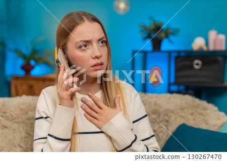 Caucasian woman sitting on sofa at home shocked and sad after receiving bad news on smartphone 130267470