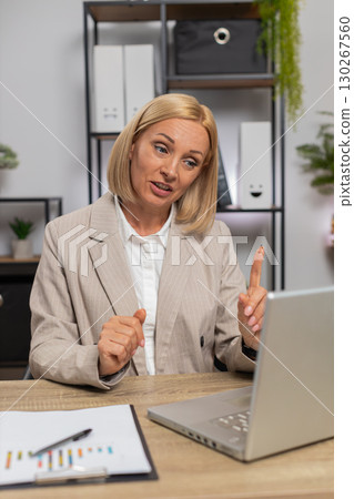 Mature businesswoman using laptop talking on online communication video call at home office desk 130267560