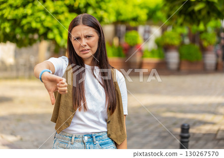 Upset young Caucasian woman lady showing double thumbs down expressing discontent on city street 130267570