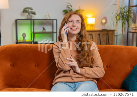 Smiling young Caucasian woman making phone conversation with friends sitting on sofa couch at home 130267571