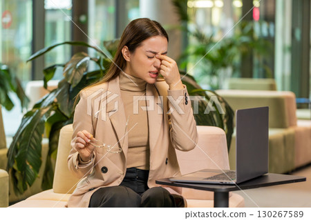 Overworked businesswoman suffering from eye strain and headache working on laptop in office lobby 130267589