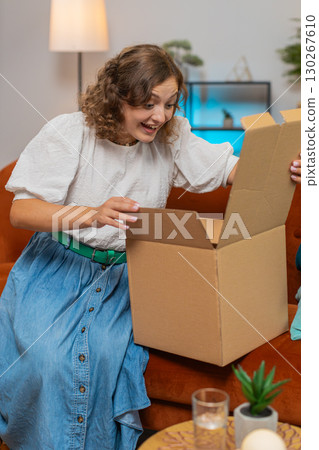 Smiling satisfied young woman shopper online shop customer opening unpacking cardboard box on sofa Smiling satisfied young woman shopper online shop customer opening unpacking cardboard box on sofa 130267610