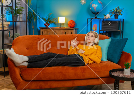 Teenager boy listening to audiobook with wireless headphones lying on sofa learning language at home Teenager boy listening to audiobook with wireless headphones lying on sofa learning language at home 130267611