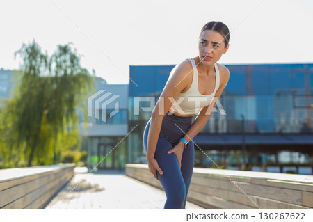 Athletic runner woman in sportswear with muscle pain after jogging in urban city park on sunny day 130267622