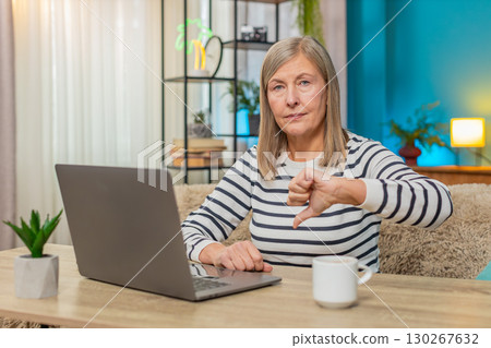 Mature woman working reading negative comment on laptop, giving thumbs down dislike dissatisfaction 130267632