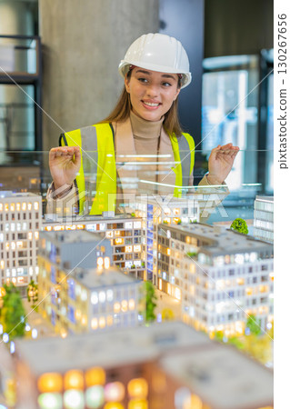 Confident young female architect in hardhat analyzing office complex architectural model in office 130267656