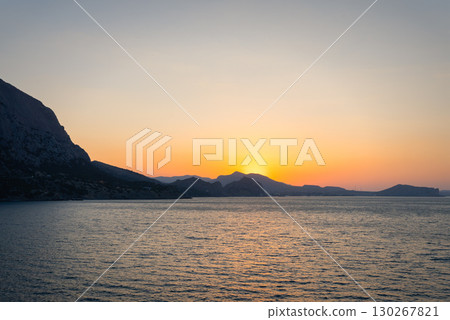 Sunrise over the sea and mountains with a soft orange sky Sunrise over the sea and mountains with a soft orange sky 130267821