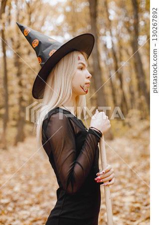 Blonde young girl witch in forest on Halloween. Girl wearing black dress and cone hat. Witch holding a broom. 130267892