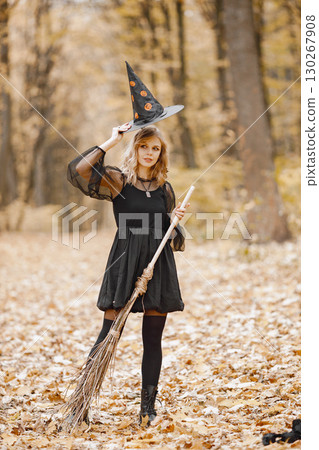 Blonde young girl witch in forest on Halloween. Girl wearing black dress and cone hat. Witch holding a broom. 130267908