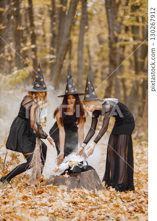 Three girls witches in forest on Halloween. Girls wearing black dresses and cone hats. Witches make a magic potion. Three girls witches in forest on Halloween. Girls wearing black dresses and cone hats. Witches make a magic potion. 130267912