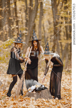 Three girls witches in forest on Halloween. Girls wearing black dresses and cone hats. Witches make a magic potion. Three girls witches in forest on Halloween. Girls wearing black dresses and cone hats. Witches make a magic potion. 130267913