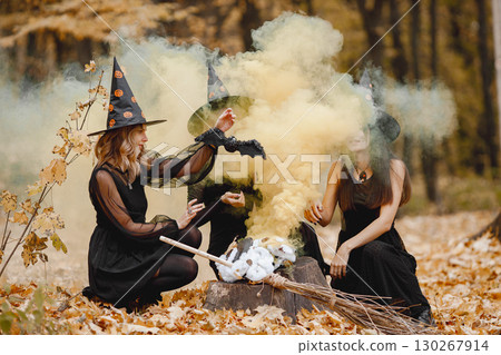 Three girls witches in forest on Halloween. Girls wearing black dresses and cone hats. Witches make a magic potion. 130267914