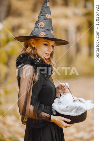 Blonde young girl witch in forest on Halloween. Girl wearing black dress and cone hat. Witch holding a magician stuff. Blonde young girl witch in forest on Halloween. Girl wearing black dress and cone hat. Witch holding a magician stuff. 130267923