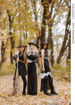 Three young girls witches in forest on Halloween. Girls wearing in black dresses and cone hat. Witch holding a magician stuff. 130267925