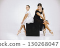 Little ballerina with her mother on white background. Brunette girl wearing white ballet suit and adult woman black dress. Two female dancer sitting on a black cube. 130268047