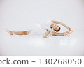 Little ballerina on white background. Brunette girl wearing white ballet suit. Girl sitting on a twine. 130268050