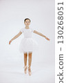 Little ballerina on white background. Brunette girl wearing white ballet suit. Girl standing on her toes. 130268051