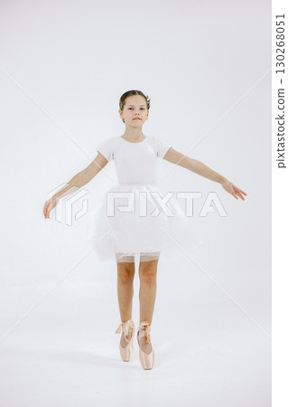 Little ballerina on white background. Brunette girl wearing white ballet suit. Girl standing on her toes. 130268051