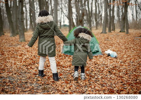 Beautiful little black girls standing near tent in the forest. Two little sisters playing in autumn forest. Black girls wearing khaki coats. 130268080