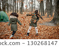 Beautiful little black girls standing near tent in the forest. Two little sisters playing with yellow leaves in autumn forest. Black girls wearing khaki coats. 130268147